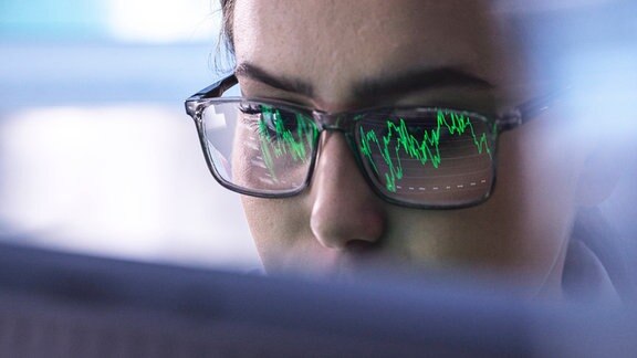 Nahaufnahme einer Frau mit Brille auf der sich ein Graph spiegelt, der auf ihrem Computer angezeigt wird.