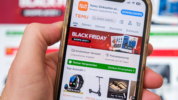 Eine Hand hält Mobiltelefon auf der die Website des chinesischen Unternehmens Temu zu sehen ist 