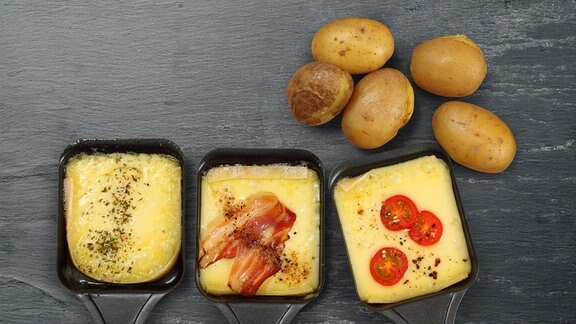 Raclettepfännchen gefüllt mit Käse, Tomaten und Speck