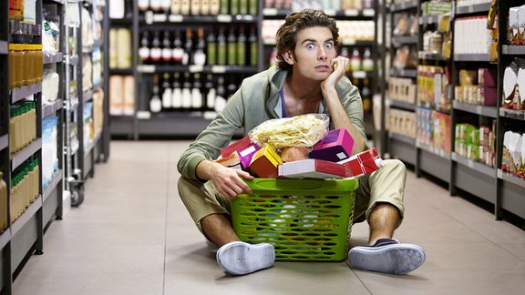 Mann sitzt gestresst auf dem Boden eines Supermarktes