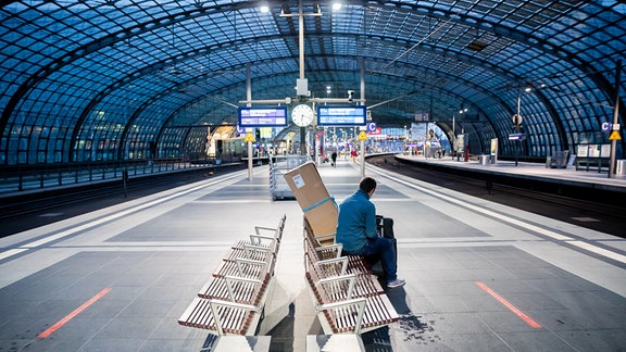 Ein Fahrgast sitzt am Morgen am Berliner Hauptbahnhof auf einem weitgehend leeren Bahnsteig