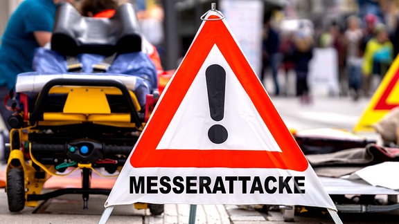 Warnschild mit Aufschrift: Messerattacke, vor Rettungskräften an einem Tatort.