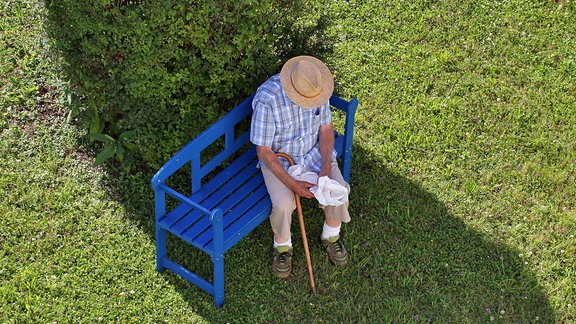 Senior sitzt im Schatten auf einer Gartenbank