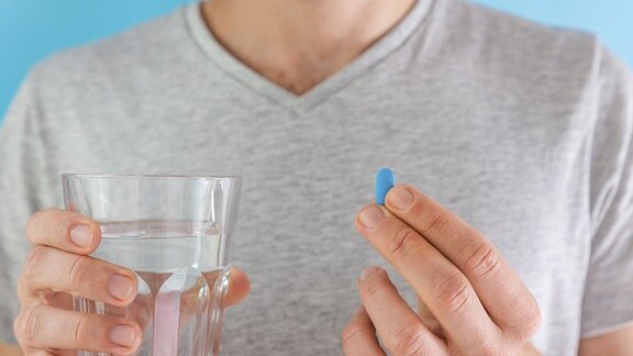 Mann trinkt eine blaue PrEP-Pille mit einem Glas Wasser. HIV-Prävention mit Medikamenten zur Präexpositionsprophylaxe.