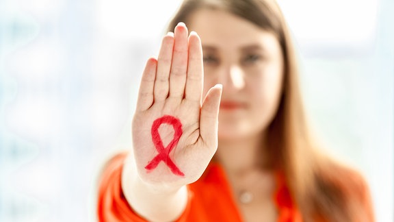 Frau streckt ihre hand nach vorn und hat die AIDS-Schleife auf ihre Handinnenfläche gemalt. 