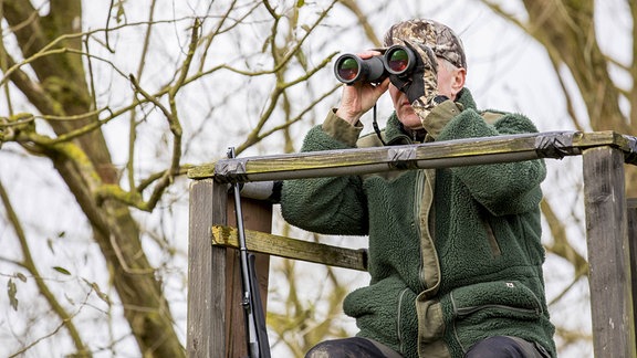Jäger auf sitzt mit einem Fernglas auf einem Hochsitz