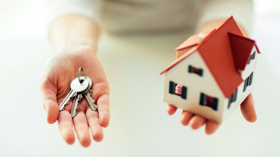 Zwei Hände halten Schlüssel und Miniaturhaus 