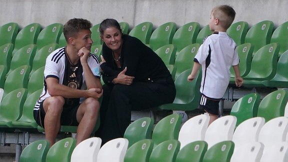 Joshua Kimmich sitzt mit seiner Frau Lina und Kind nach einem Spiel auf der leeren Tribüne. Aufnahme vom 12.06.2023