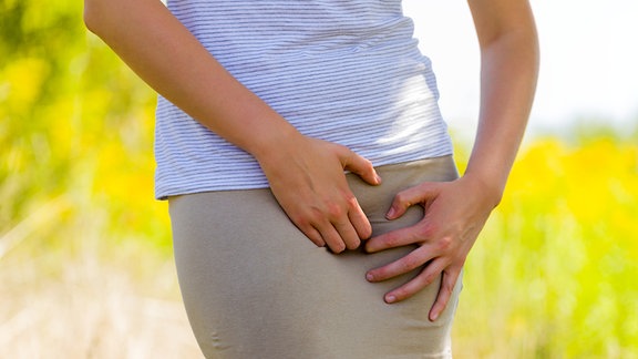 Frau kratzt sich im Freien wegen einer Infektion die Vagina im Rock.