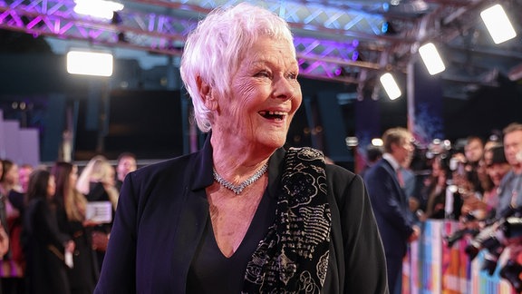 Judi Dench posiert lachend für die Kamera.