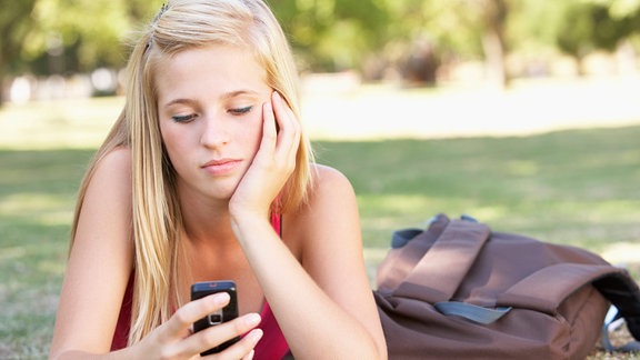 Mädchen schaut gelangweilt auf Mobiltelefon