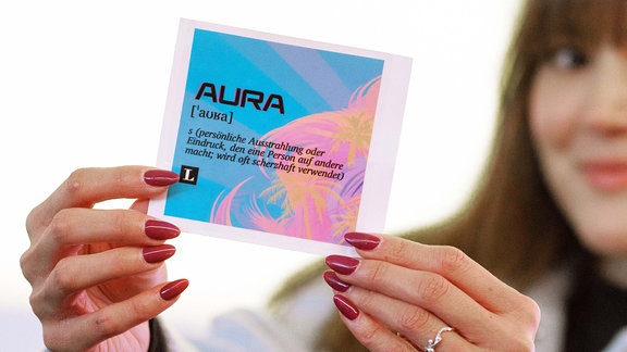 Patricia Kunth, Projekt-Managerin Jugendwort / PONS Langenscheidt, hält einen Aufkleber mit dem Jugendwort 2024 "Aura". "Aura" ist das Jugendwort des Jahres 2024. 