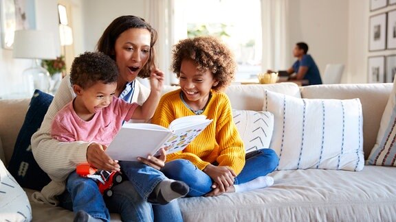 Eine Frau liest einem Mädchen und einem Jungen aus einem Buch vor