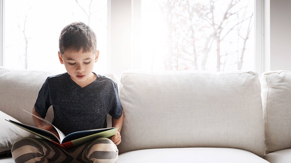 Junge sitzt auf dem Sofa und schaut ein Buch an.