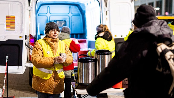 Eine ehrenamtliche Helferin überreicht bei frostigen Temperaturen am Kältebus der Caritas einen Becher