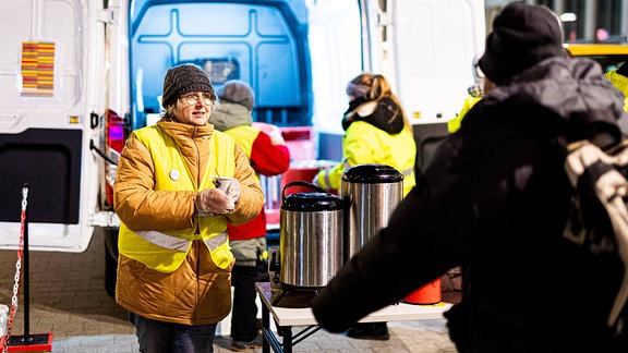Eine ehrenamtliche Helferin überreicht bei frostigen Temperaturen am Kältebus der Caritas einen Becher Kaffee.