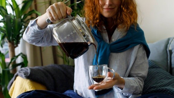 Frau gießt Kaffee in eine Tasse.