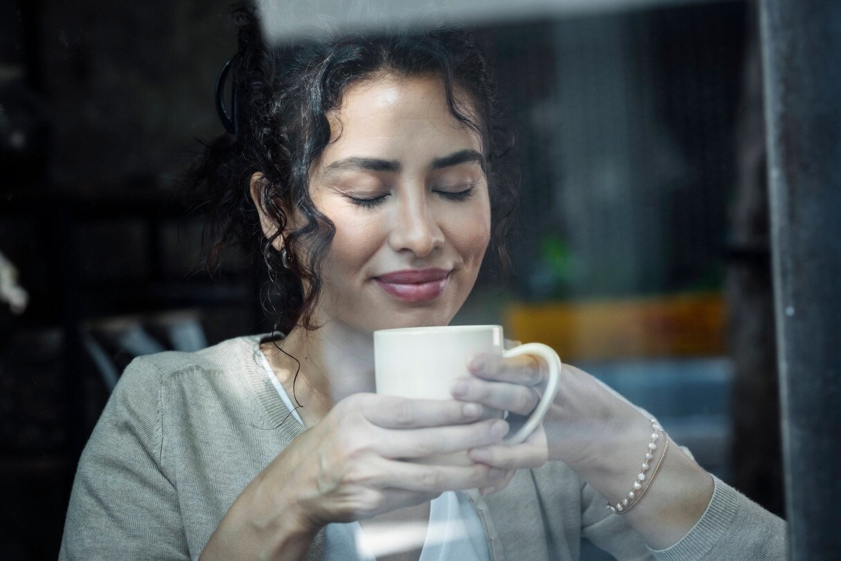 Eine Frau mit geschlossenen Augen hält eine Tasse Kaffe.