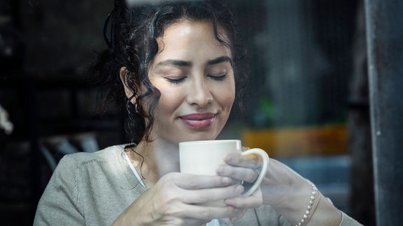 Eine Frau mit geschlossenen Augen hält eine Tasse Kaffe.