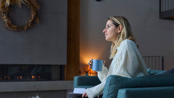 Eine Frau mit Kaffeetasse sitzt zu Hause.