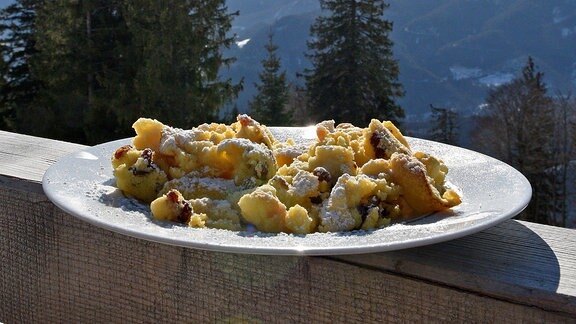 Ein Teller mit Kaiserschmarrn auf einer Brüstung, dahinter eine Berglandschaft