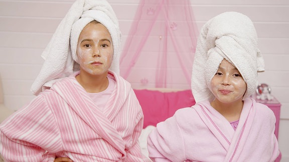 Zwei Mädchen mit Gesichtsmasken tragen Handtuchturbane und Bademäntel