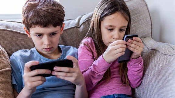 Zwei Kinder schauen auf Smartphones.