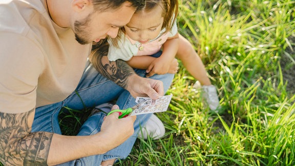 Ein Mann und ein Kind schneiden ein Klebetattoo aus einem Tattoo-Bogen.