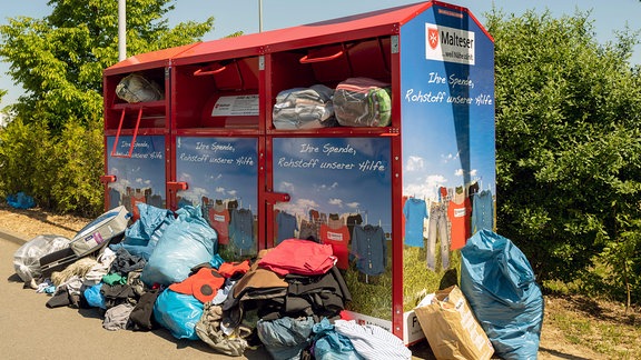 Malteser Kleidercontainer läuft über, Säcke mit Altkleidern liegen davor.