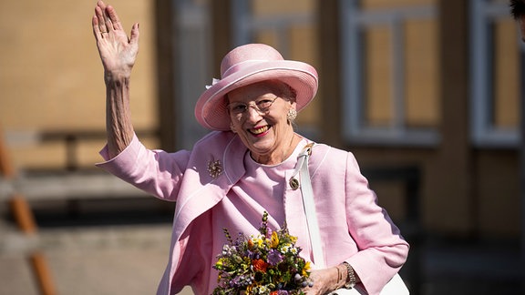 Die dänische Königin hält einen Blubenstrauß in ihrer Linken und winkt.
