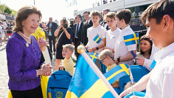 Königin Silvia von Schweden begrüsst vor einem Schiff der Weißen Flotte bei einer Benefizveranstaltung zugunsten der World Childhood Foundation Kinder mit schwedischen Flaggen in den Händen.