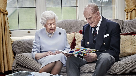 Die britische Königin Elizabeth II. und ihr Ehemann Prinz Philip, Herzog von Edinburgh, sitzen im Oak Room im Schloss Windsor. Sie sehen sich selbstgebastelte Hochzeitstagskarten an, die sie von ihren Großenkeln anlässlich ihres 73. Hochzeitstages geschenkt bekommen haben.