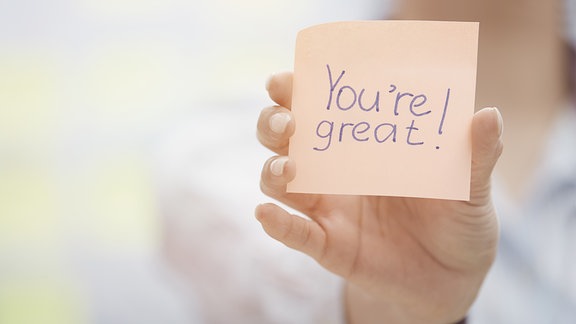 Eine Hand hält einen Zettel auf dem steht "You're great!"