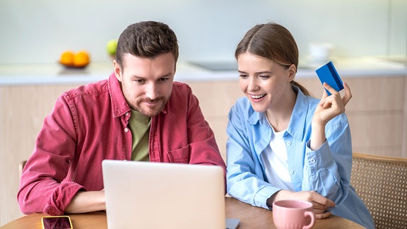 Ein junger Mann und eine junge Frau sitzen an einem Tisch vor einem Laptop