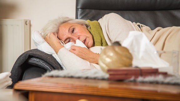Eine ältere Frau liegt krank auf einer Couch.