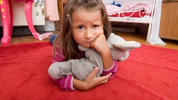Ein fünfjähriges Mädchen liegt mit dem Stofftier auf dem Boden