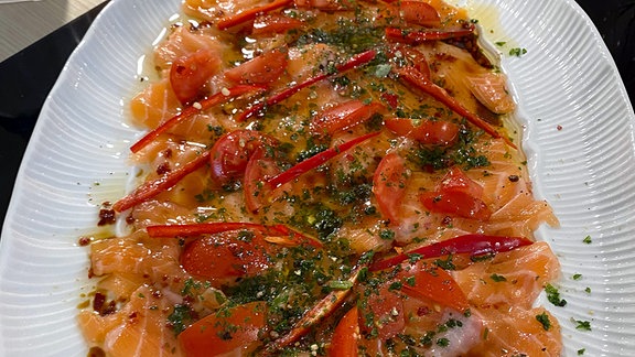 Lachs-Carpaccio auf einer weißen ovalen Platte angerichtet.