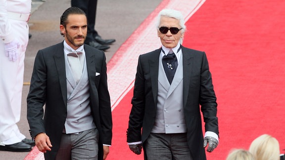 Das französische Model Sebastien Jondeau (L) und der deutsche Designer Karl Lagerfeld (R) kommen zur Hochzeitsmesse von Fürst Albert II. von Monaco und Fürstin Charlene im Haupthof des Fürstenpalastes in Monaco, 2011.