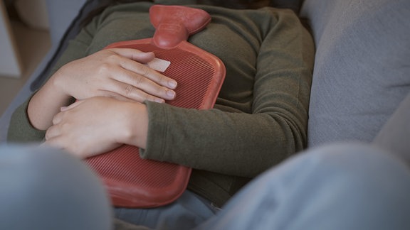 Eine Frau hält sich eine Wärmflasche auf den Bauch