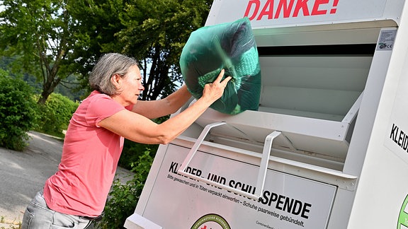 Eine Frau wirft eine Kleiderspende in einen Altkleidungscontainer