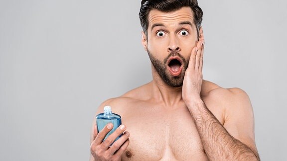 Schockierter Mann hält Flasche mit Aftershave-Lotion und berührt Gesicht.