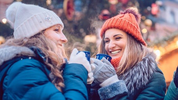 Zwei Frauen trinken Glühwein auf einem Weihnachtsmarkt.