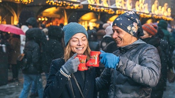 Eine Frau und ein Mann mit Glühwein auf einem Weihnachtsmarkt