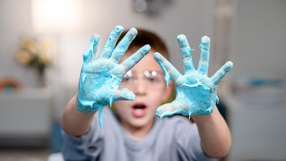 Ein Junge zeigt seine mit blauen Spielschleim überzogenen Hände.