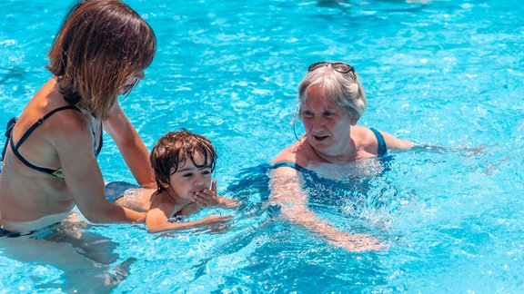 Symbolbild: Zwei Frauen in einem Schwimmbad, zwischen ihnen schwimmt ein Kind.