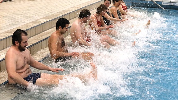 Erwachsene  strampeln am Beckenrand mit den Beinen im Wasser.