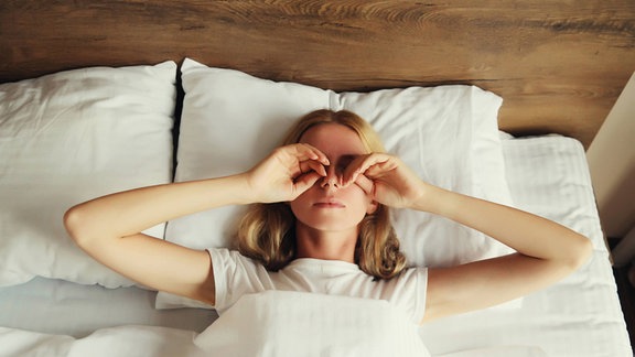 Eine Frau liegt rücklings im Bett und reibt sich die Augen.