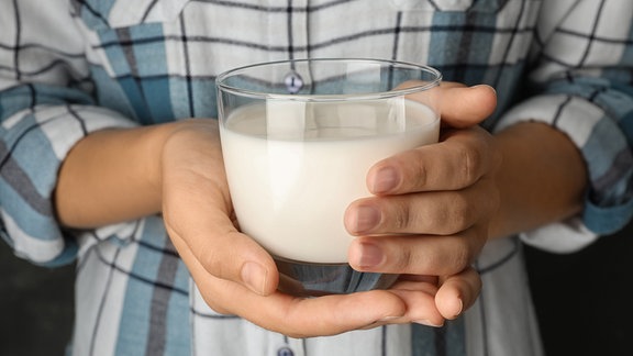 Hände halten ein Glas Milch.