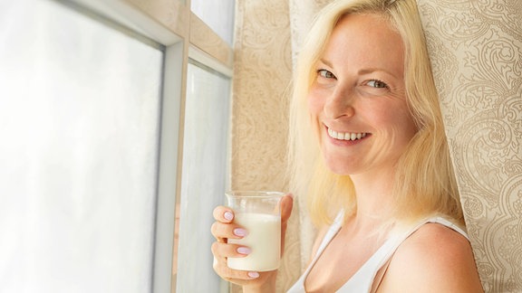 Eine Frau hält ein Glas Milch in der Hand und lächelt.