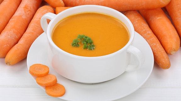 Möhrensuppe in Suppentasse vor rohen Möhren